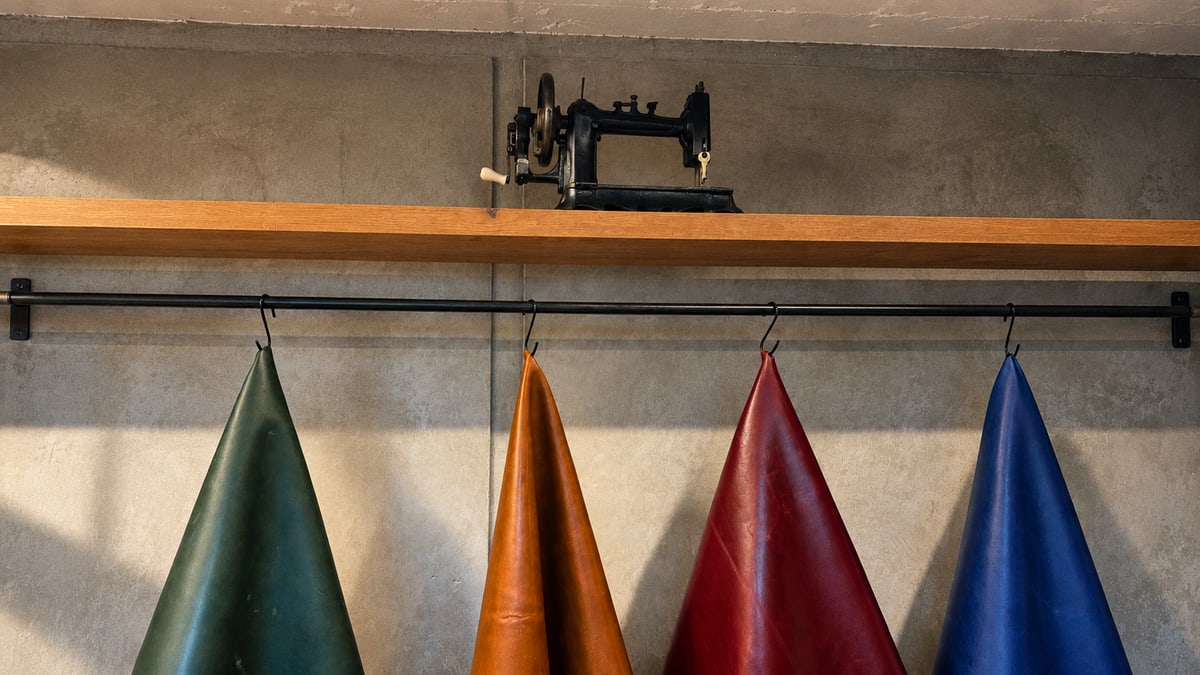 Pieles de colores colgadas en el taller, bajo una máquina de coser antigua.