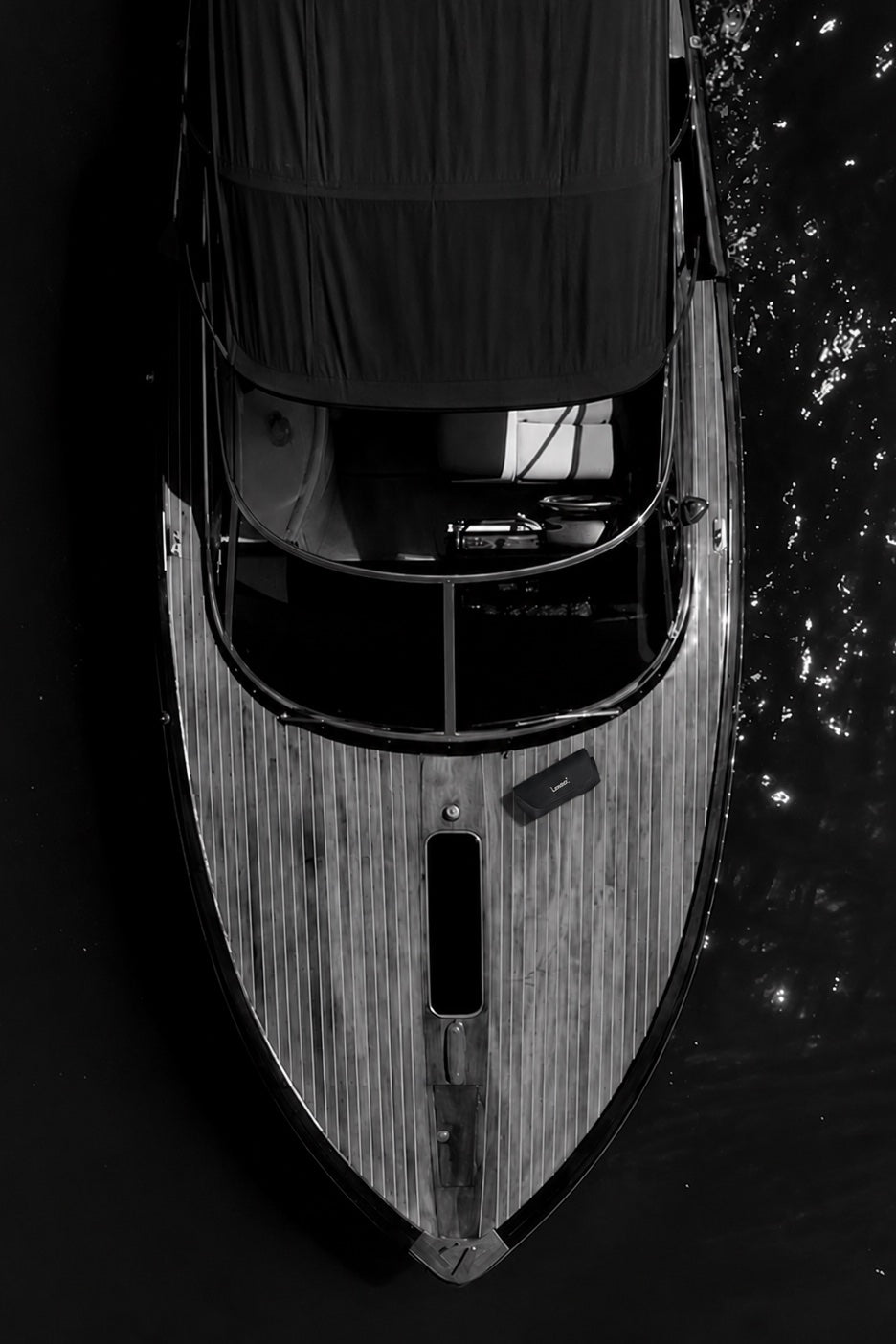 Una lancha de madera vista desde arriba, en blanco y negro, con un estuche de Lenso sobre la cubierta y el agua oscura alrededor.