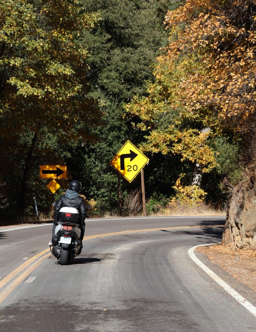 Alguien en moto tomando una curva de una carretera de montaña, entre árboles de otoño.