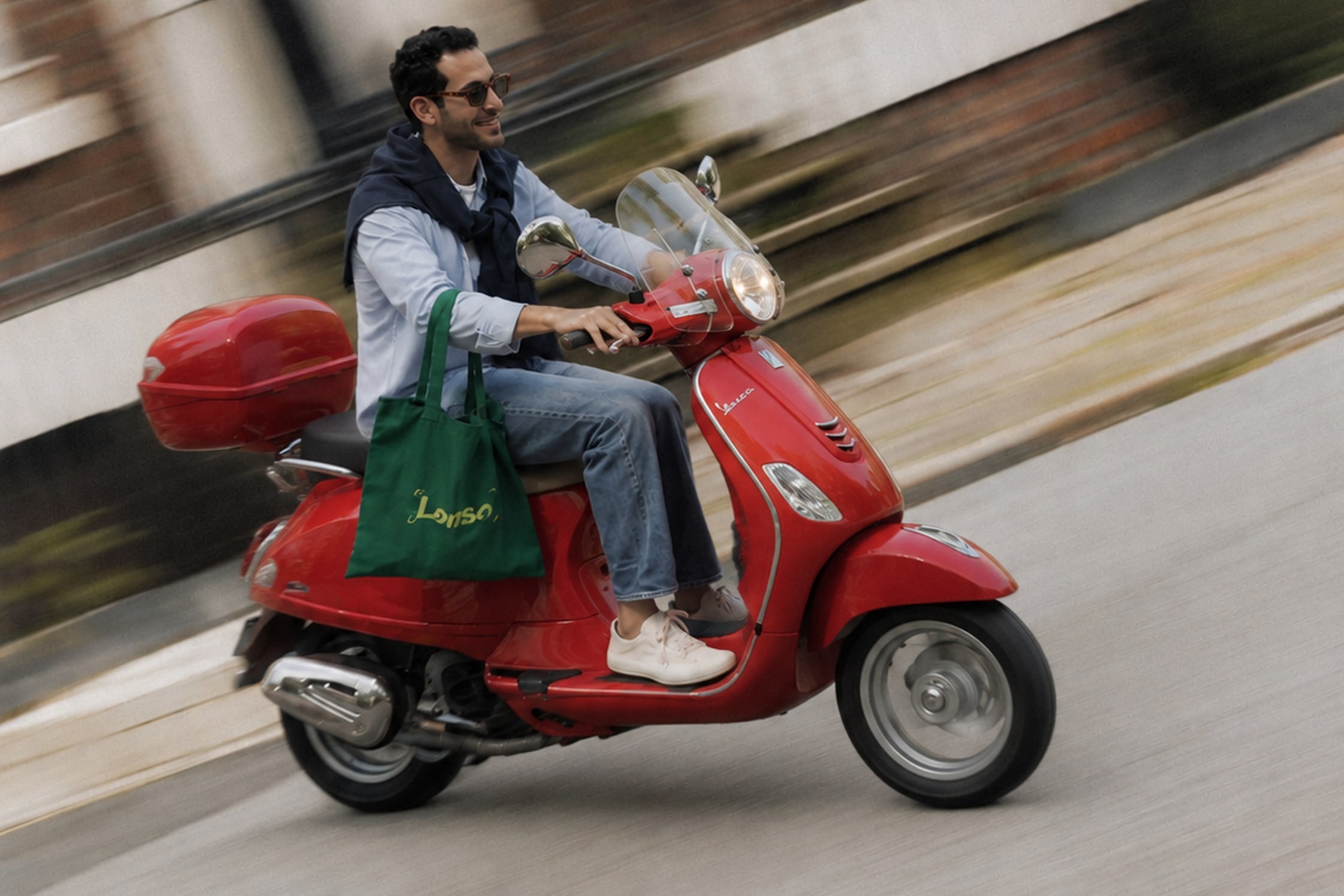 Un hombre en una moto roja por la ciudad, con una bolsa verde de Lenso colgada del manubrio y el fondo barrido por el movimiento.