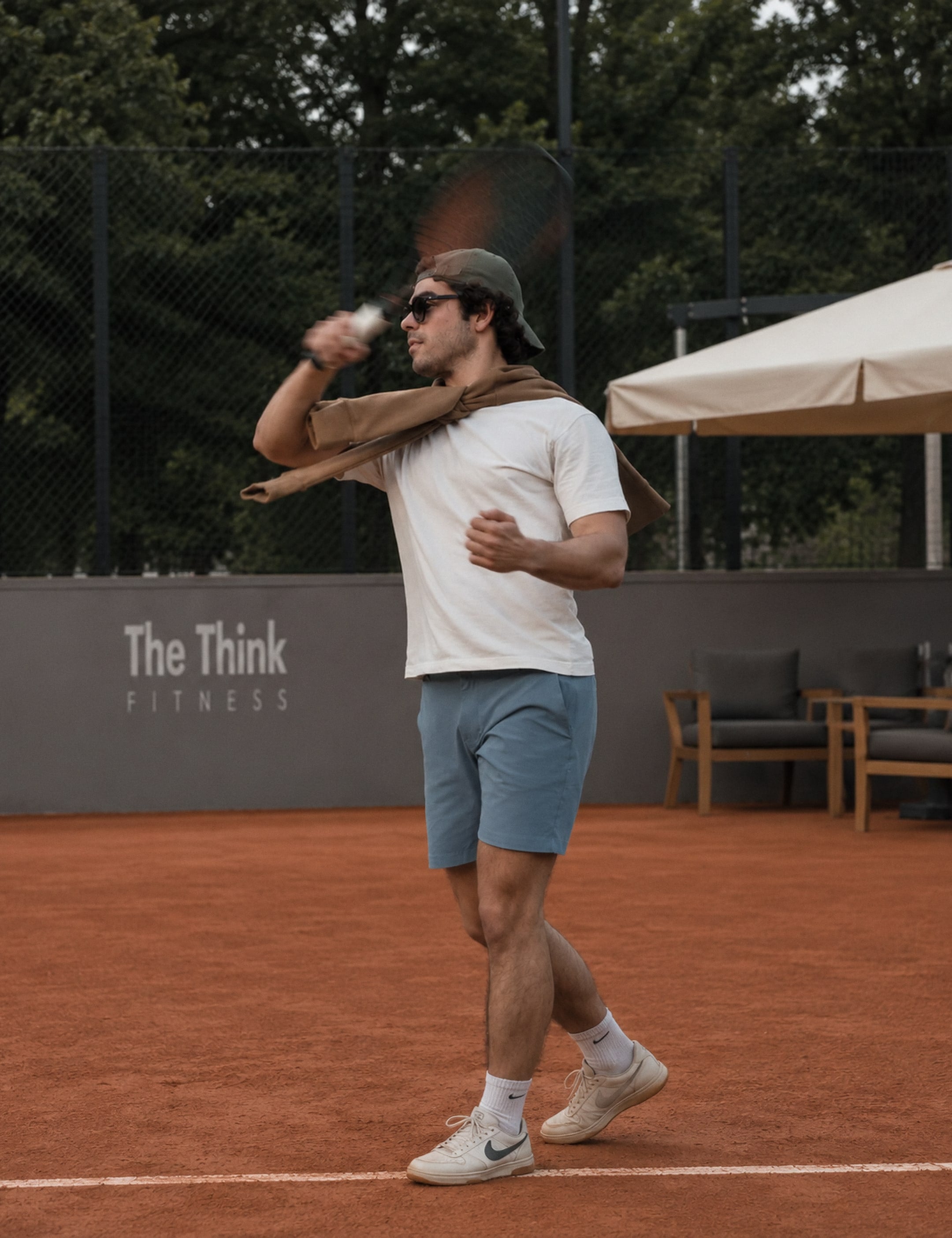 Alguien terminando un golpe de raqueta en una cancha de arcilla, con gorra y lentes de sol.